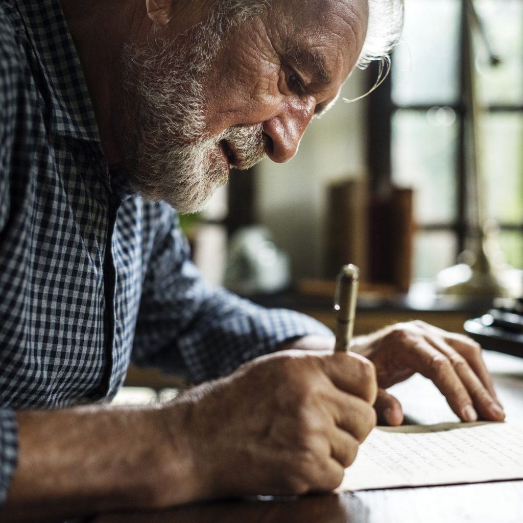 Senior man writing in blank greeting card.